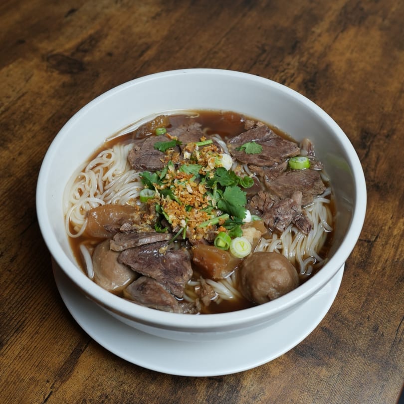 Nalak Thai's beef noodle soup with sliced beef, meatballs, and herbs in a white bowl.