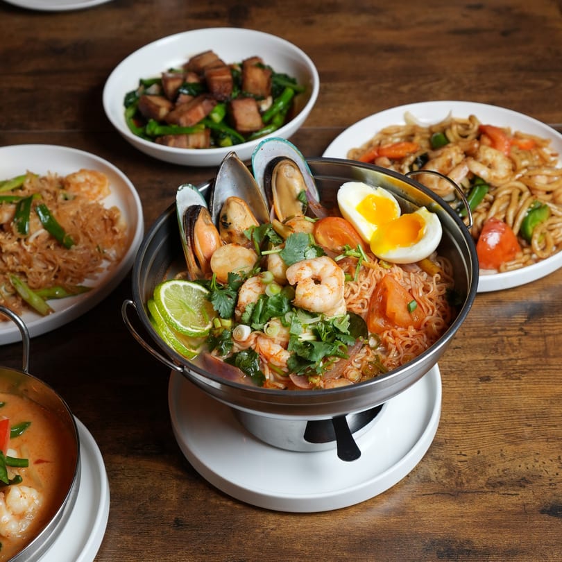 A table spread of Nalak Thai dishes, including a seafood noodle bowl, fried rice, and stir-fry.