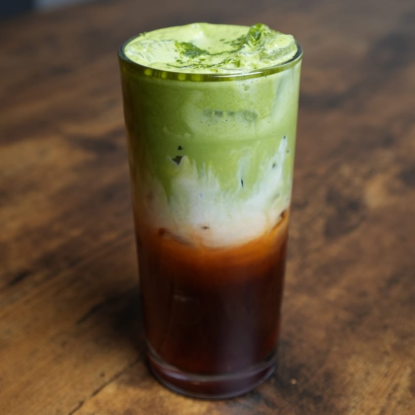 Layered Nalak Thai iced matcha latte with brown, white, and green sections on a wooden table.