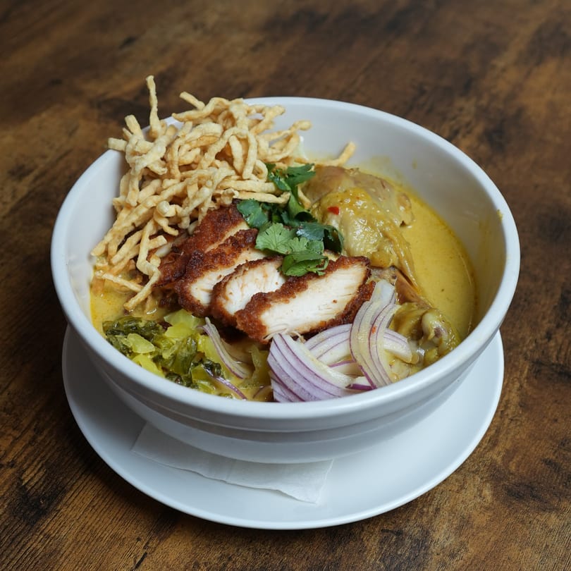 Nalak Thai's Khao Soi with crispy and soft noodles, chicken, red onions, and cilantro in a rich curry broth.